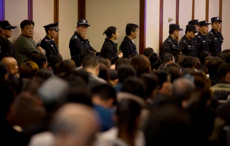 In this March 27, 2014 file photo, Chinese policemen stand watching the relatives of Chinese passengers on board Malaysia Airlines Flight 370 as they attend a briefing by Malaysian officials at a hotel in Beijing, China. (AP Photo/Andy Wong, File)