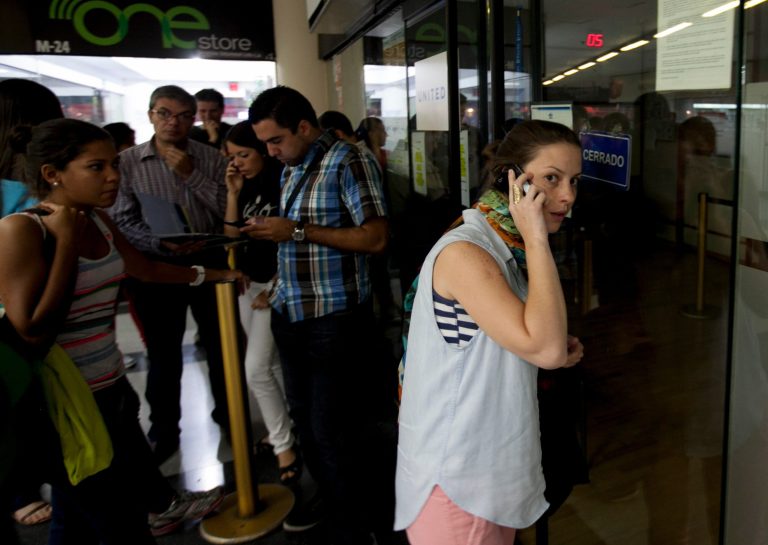 A woman speaks on her cell as she seeks information about flight sales from a closed United Airlines office in Caracas, Venezuela, Friday, Jan. 24, 2014.  Delta, American Airlines and Panama's Copa Airlines were also among carriers whose offices were either closed or had halted sales on Friday after the government devalued the local currency for flights abroad. (AP Photo/Alejandro Cegarra)