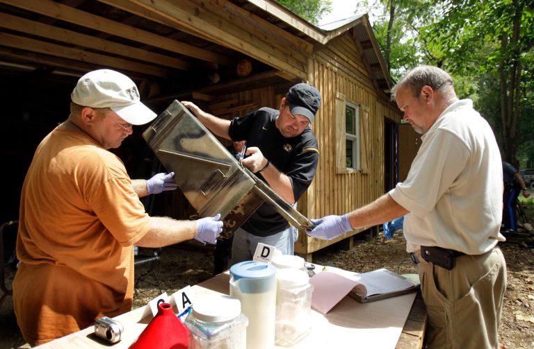   FILE - In this Sept. 2, 2010 file photo, Franklin County Detective Jason Grellner, center, sorts through evidence with Detective Darryl Balleydier, left, and reserve Officer Mark Holguin during a raid of a suspected meth house in Gerald, Mo. Methamphetamine lab seizures are on the rise in the nation's cities and suburbs, raising new concerns about a lethal drug that has long been the scourge of rural America. (AP Photo/Jeff Roberson, File)  