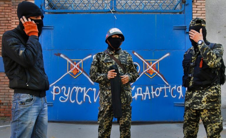 Pro Russian militants stand in front of a gate with graffiti reading 