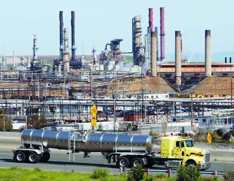 FILE - This March 9, 2010 file photo shows a tanker truck passing the Chevron oil refinery in Richmond, Calif. On Weds., Nov. 14, 2012, California's largest greenhouse gas emitters will for the first time begin buying permits in a landmark 
