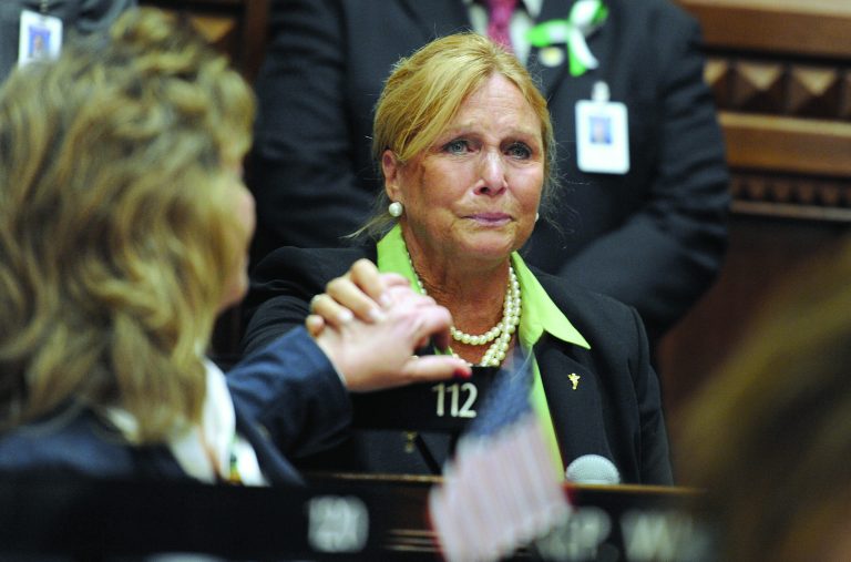FILE - In this Wednesday, Dec. 19, 2012 file photo, State Rep. DebraLee Hovey, R-112 district, including Newtown, grabs the hand of colleague Rep. Laura Hoydick, R-Stratford, left, after speaking at a memorial service for the victims of the Sandy Hook Elementary School shooting before the House of Representatives and Senate meet for special session the state Capitol. Hovey has apologized after saying in a Facebook post that shooting victim and former Arizona U.S. Rep. Gabrielle Giffords should 
