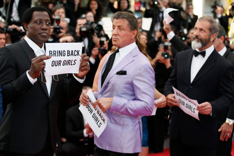 From left, the cast of The Expendables Wesley Snipes, Sylvester Stallone, and Mel Gibson hold up banners reading, 