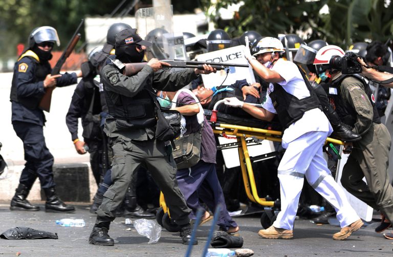 An armed Thai police officer, center, aims his rubber bullet rifle as medical team carry a injured person on a stretcher during a clash between police force and anti-government protesters Tuesday, Feb. 18, 2014 in Bangkok, Thailand. Clashes between police and anti-government demonstrators in Bangkok left two people dead and 57 others injured Tuesday as riot police attempted to clear out protest camps around the Thai capital. (AP Photo/Apichart Weerawong)