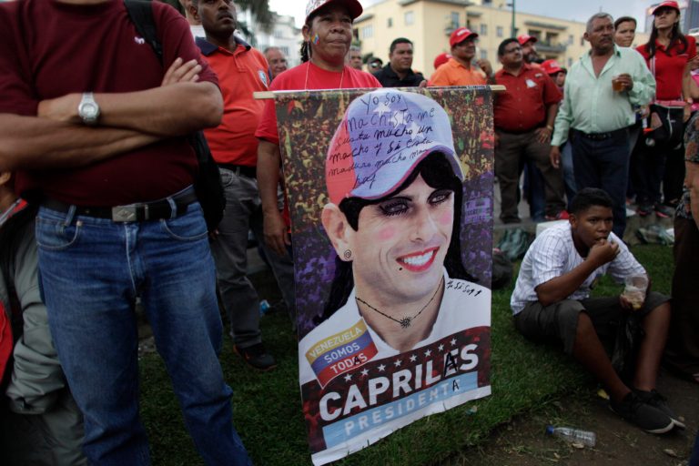 In this photo taken May 1, 2013, supporters of the ruling party stand around a defaced poster of opposition presidential candidate Henrique Capriles during a May Day march in Caracas, Venezuela. Venezuelans have long been obsessed by politics, especially during the Chavez years, as the populist leader denounced his opponents as 