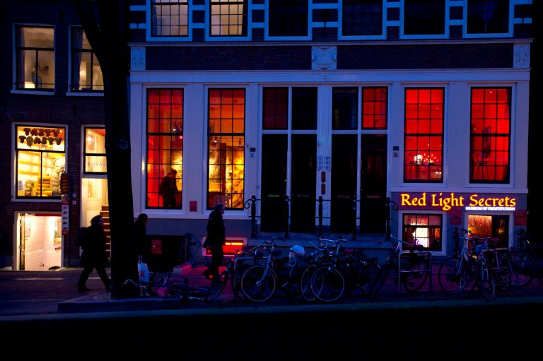 In this photo taken Tuesday, Feb. 4, 2014, the entrance of the 'Red Light Secrets' prostitution museum is seen, right, in Amsterdam. On any given evening, thousands of tourists stroll down the narrow streets of Amsterdam's famed Red Light District, gawking at ladies in lingerie who work behind windows, making a living selling sex for money. Now a small educational museum is opening in heart of the district that aims to show reality from the other side of the glass. Organizer Melcher de Wind says the Red Light Secrets museum is for those who want to learn more about how the area works without actually visiting a prostitute. (AP Photo/Evert Elzinga)