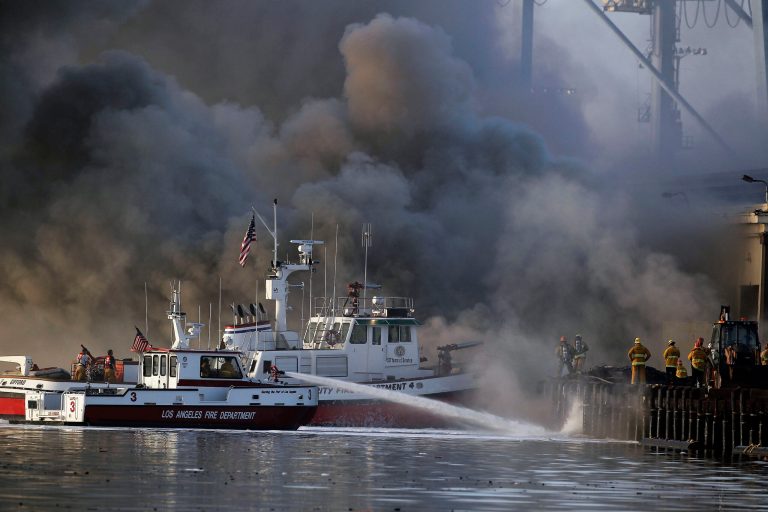 Los Angeles firefighters watch as smoke from a dock fire continues to rise at the Port of Los Angeles in the Wilmington section of Los Angeles on Tuesday, Sept 23, 2014. The fire that forced evacuations from the wharf continues to smolder but officials say it's under control. Nearly 12 hours after starting, the blaze is sending up huge plumes of smoke that is drifting over Los Angeles Harbor early Tuesday. (AP Photo/ Nick Ut )