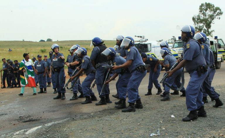 Police officers stand on guard as residents protest at Zithobile in Bronkhorstspruit, near Pretoria, South Africa, Thursday, Feb. 6, 2014. Demonstrators set several buildings, including a clinic, on fire on Wednesday in the Bronkhorstspruit district, east of the capital, Pretoria, to protest what they say are high electricity prices. (AP Photo/Themba Hadebe)