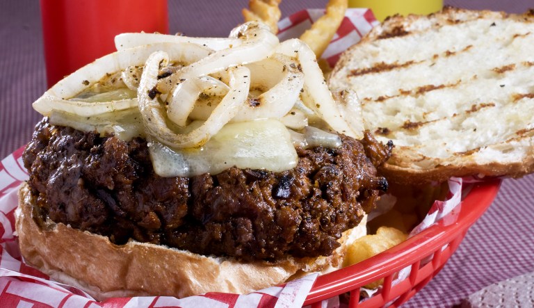 A cheeseburger with onions is seen on a plate next to some fries, ketchup, and mustard.