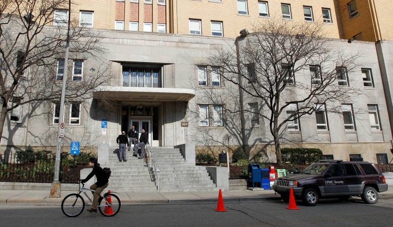 A cyclist rides by as security guards keep watch at the front entrance to the Western Psychiatric Institute and Clinic on the University of Pittsburgh campus in Pittsburgh.