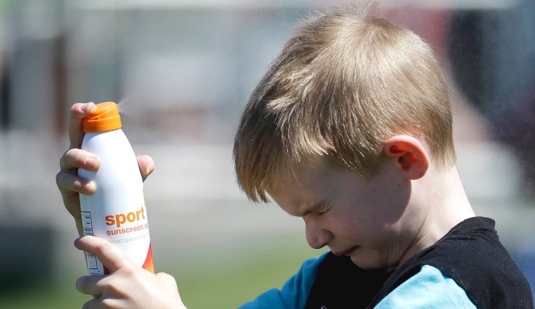 Landon Tapper sprays sunscreen on his face.