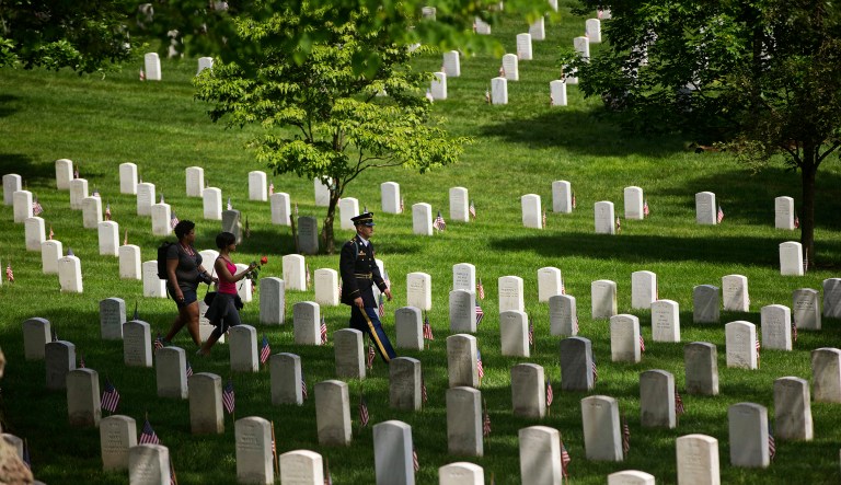 A member of the U.S. Army's 3rd Infantry Regiment "The Old Guard" walks with visitors among the graves at Arlington National Cemetery, Monday, May 30, 2016 in Arlington, Va.