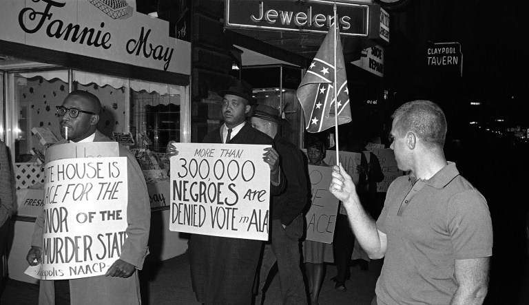 In this April 14, 1964, photo, a man holds a Confederate flag as demonstrators march in front of an Indianapolis hotel where then-Alabama Governor George Wallace was staying.