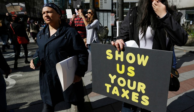 A woman in Seattle holds a sign during a rally that reads "Show us your taxes" in reference to calls for President Trump to release his tax returns, so Americans can scrutinize his business ties and potential conflicts of interest.