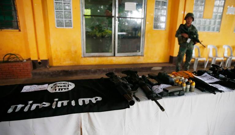 A Philippine Marine guards the display of recovered high-powered firearms, ammunitions, uniforms and black ISIS-style flags which were shown to reporters Tuesday, May 30, 2017 in Marawi city southern Philippines. Philippine forces pressed their offensive to drive out militants linked to the Islamic State group after days of fighting left corpses in the streets and hundreds of civilians begging for rescue from a besieged southern city of Marawi. 