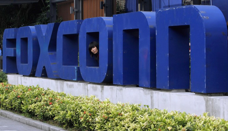 FILE - In this May 27, 2010 file photo, a worker looks out through the logo at the entrance of the Foxconn complex in the southern Chinese city of Shenzhen. Wisconsin Assembly Democratic Leader Peter Barca was branded as failing "on all accounts" by a fellow Democrat who was "incredibly frustrated and concerned" with his actions after Barca joined Republicans in voting for a $3 billion tax incentive package for Foxconn Technology Group. Barca was one of three Democrats to vote for the measure Thursday, Aug. 17, 2017, with 28 Democrats against. 