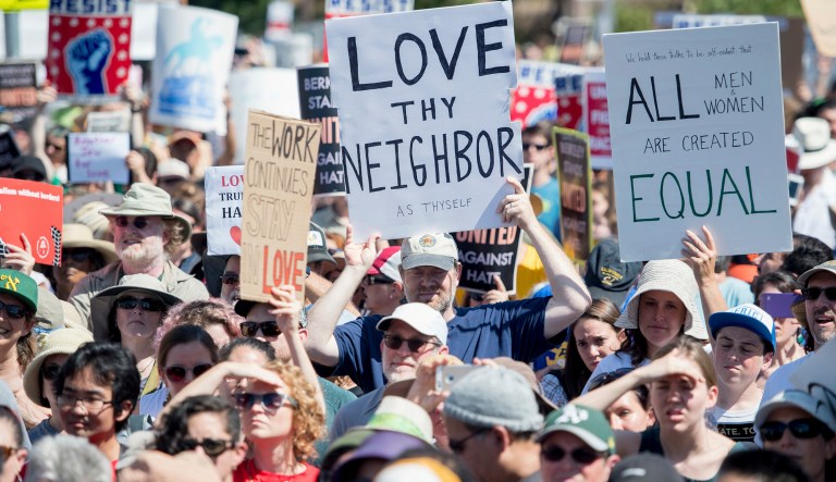 People hold up signs and shout while listening to speakers during a rally against hate. 