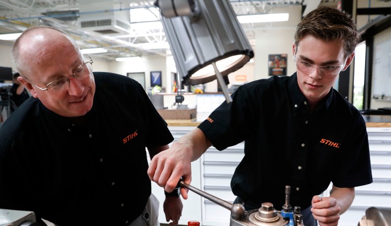 Apprentice Ryan Buzzy, right, works with Skip Johnson, a trainer for the Stihl Inc. apprenticeship program, on a metalworking lathe in their training area at the Stihl Inc. manufacturing facility in Virginia Beach, Va.