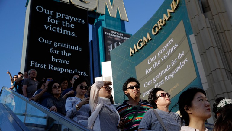 People take an outdoor escalator past a sign asking for prayers for the dead outside of the MGM hotel in Las Vegas.