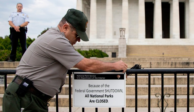 A U.S. Park Police officer watches at left as a National Park Service employee posts a sign on a barricade closing access to the Lincoln Memorial in Washington, D.C.