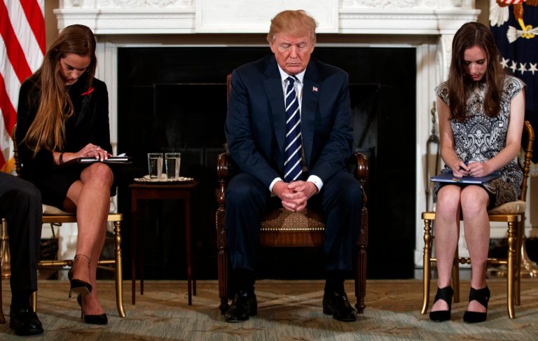 President Donald Trump, joined by student Carson Abt, right, bow their heads during the opening prayer of a listening session with high school students and teachers.