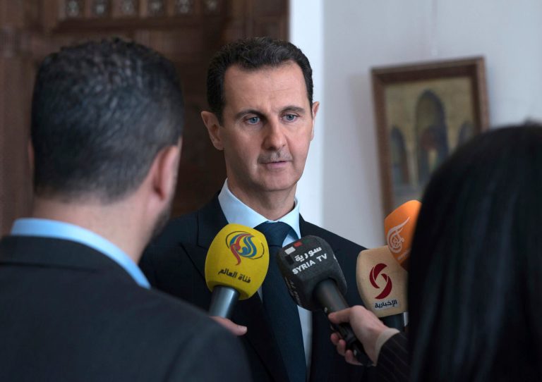 In this March 4, 2018 file photo provided by the official Facebook page of the Syrian Presidency, Syrian President Bashar Assad, center, speaks with reporters, in Damascus, Syria. In comments published on the official presidency Telegram channel Wednesday, March 14, 2018, Assad said his country's war on terrorism will continue as long as there is "a single terrorist" on Syrian territories and will go side by side with his efforts to stand up to "western scenarios that aim to undermine the country's unity and sovereignty."