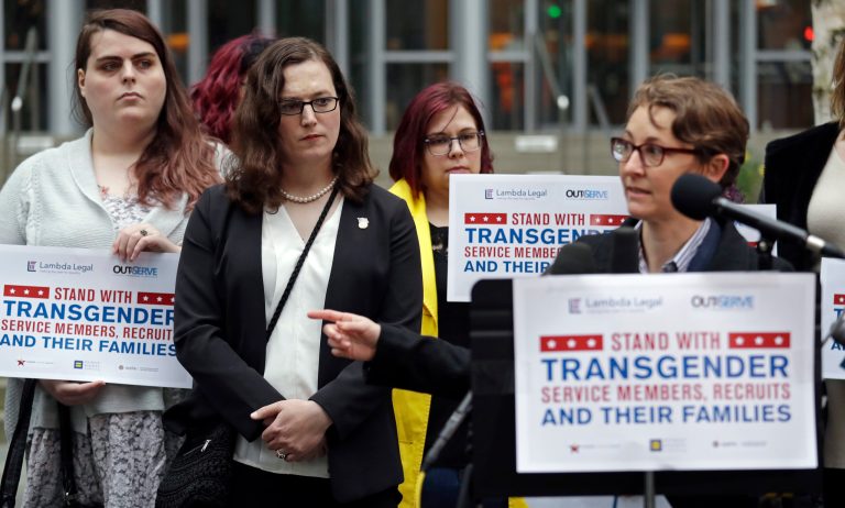 Plaintiff Cathrine Schmid, second left, listens as attorney Natalie Nardecchia speaks to media members in front of a federal courthouse following a hearing there Tuesday, March 27, 2018, in Seattle. U.S. District Judge Marsha Pechman says she won't immediately consider President Donald Trump's new policy banning transgender people from serving in the military. Pechman is one of four federal judges who have issued orders blocking Trump's decision last year to overturn an Obama-era directive allowing transgender troops to serve openly.
