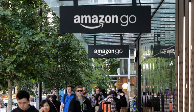 In this Monday, May 7, 2018 photo, pedestrians and cyclists gather near the Amazon Go store, in Seattle. Seattle's latest tax proposal to combat homelessness takes aim at large businesses such as Amazon that have helped drive the city's economic boom. But businesses and others say the so-called head tax is misguided and potentially harmful and they question whether the city is effectively using the tens of millions of dollars it already spends on homelessness each year.