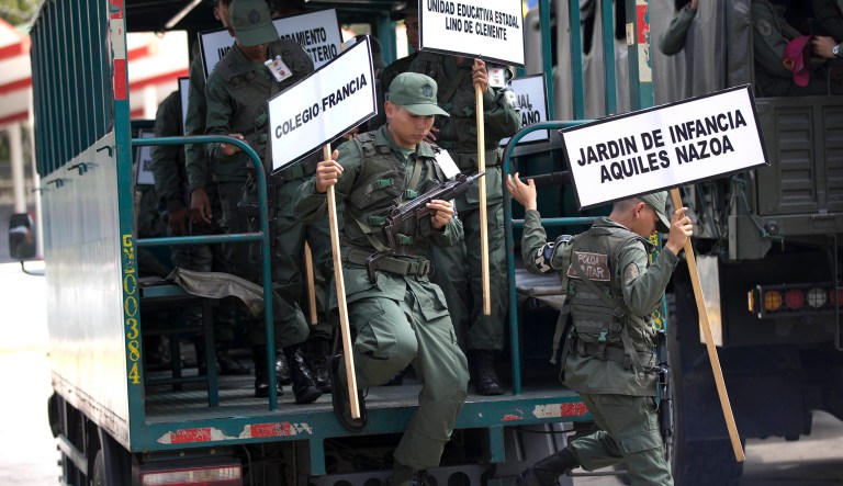 Soldiers carrying signs with the names of schools that will serve as voting centers, exit a military truck as they arrive for a ceremony at the Military Academy in Caracas, Venezuela, Tuesday, May 15, 2018. About 300,000 soldiers are in charge of security and logistics in the electoral process in the May 20 presidential election. 