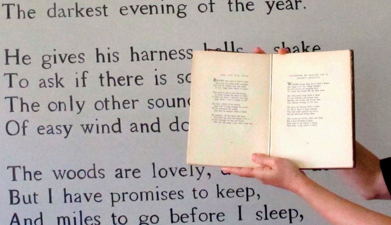 Megan Mayhew Bergman, director of the Robert Frost Stone House Museum in Shaftsbury, Vt., stands in front of the famous Frost poem, "Stopping By Woods on a Snowy Evening," painted on a wall of the museum while holding a book.
