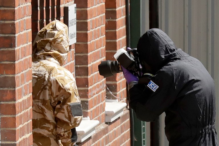 A member of a specialist team wearing a protective police suit takes a picture in the front doorway as they search the fenced-off John Baker House for homeless people on Rollestone Street in Salisbury, England, on Friday. British police are scouring sections of Salisbury and Amesbury in southwest England, searching for a container feared to be contaminated with traces of the deadly nerve agent Novichok.