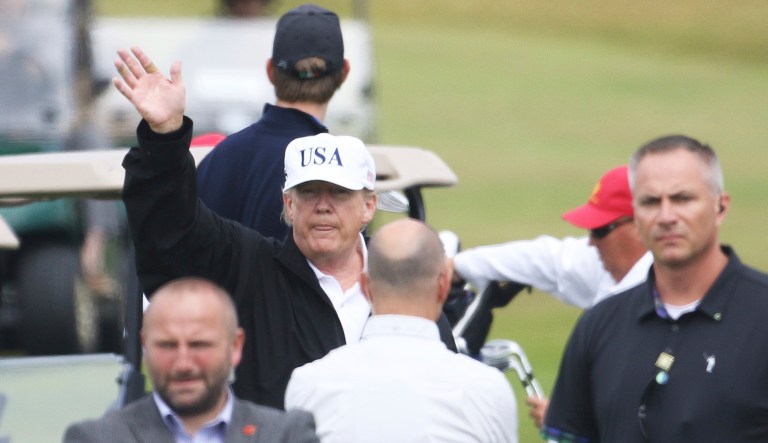 President Trump waves to protesters while he plays golf at Turnberry golf club, Scotland, on Saturday. Trump is spending the weekend at his sea-side Trump Turnberry golf resort in Scotland, where aides had said he would be busy preparing for his Monday summit in Helsinki, Finland.