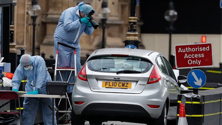 Forensics officers work near the car that crashed into security barriers outside the Houses of Parliament in London.