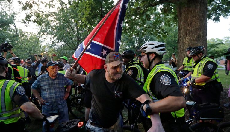 A police officer grabs a man holding a Confederate flag during a rally regarding the recently vandalized Confederate monument known as Silent Sam at the University of North Carolina in Chapel Hill, N.C., Thursday, Aug. 30, 2018. 