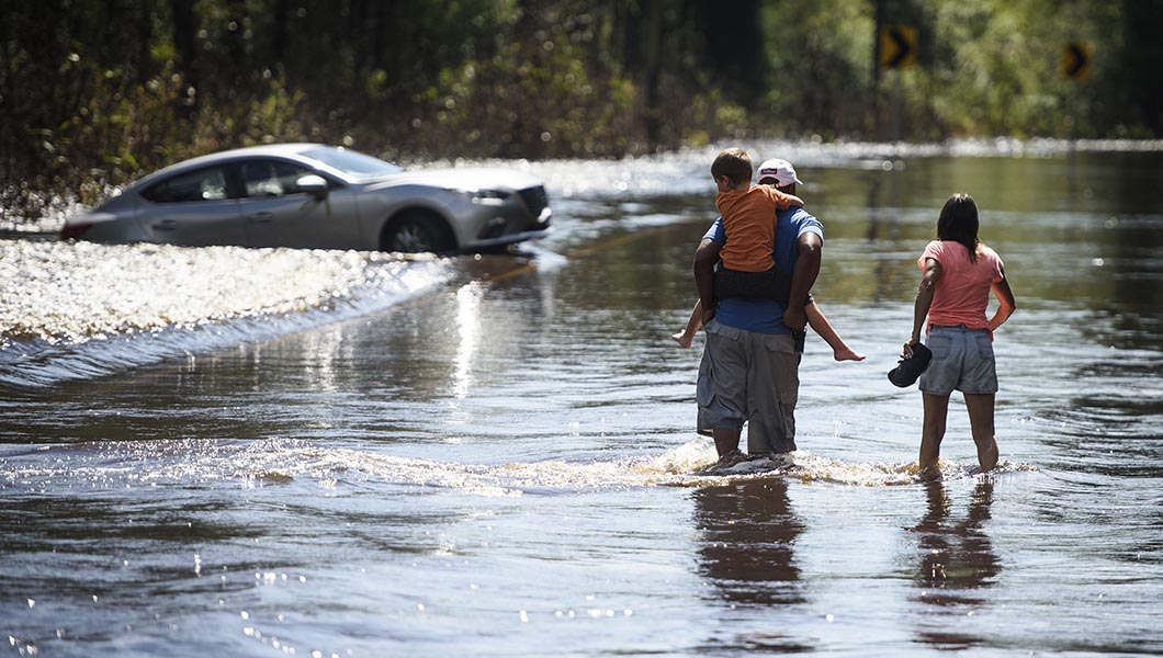 Regina Matthews, right, and a man and his child walk across a flooded Elliott Bridge Road in Linden, N.C.