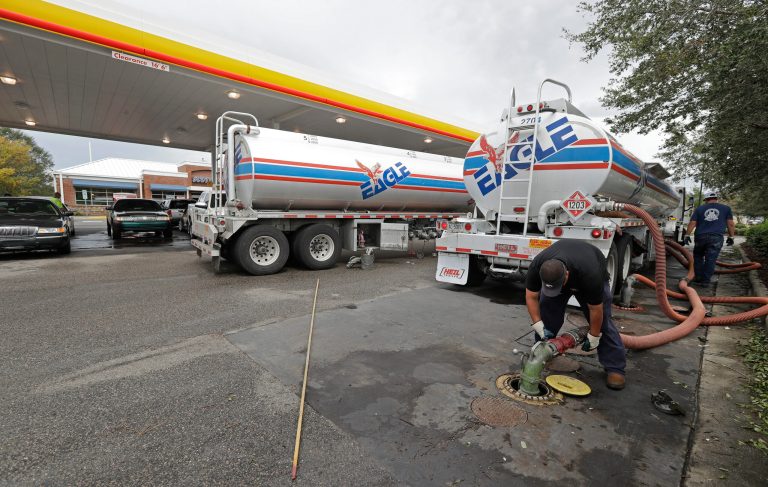 In this Sept. 17, 2018, file photo people wait in line as Travis Hall, right, and Brandon Deese, back, pump fuel from two tanker trucks at a convenience store in Wilmington, N.C.  America's rediscovered prowess in oil production is shaking up old notions about the impact of higher crude prices on the U.S. economy.