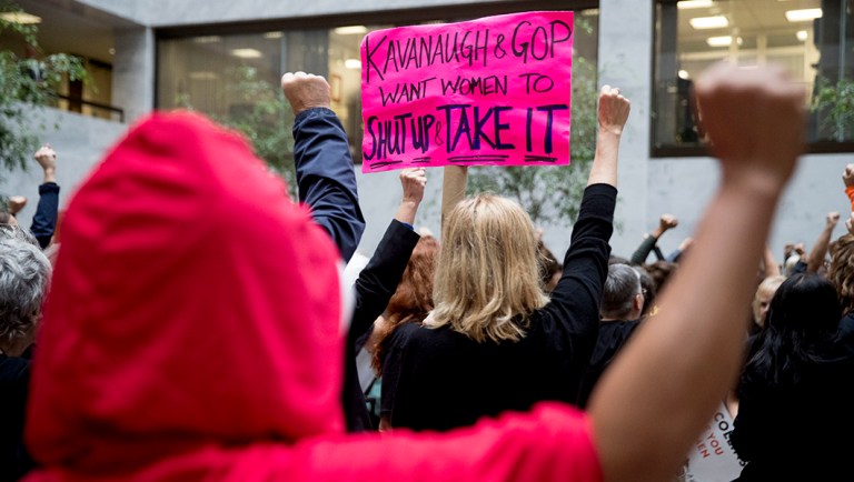 A protester of Supreme Court nominee Brett Kavanaugh wears a costume from the show "The Handmaid's Tale," and another protester holds up a sign that reads "Kavanaugh and GOP Want Women to Shut Up and Take It" on Capitol Hill.