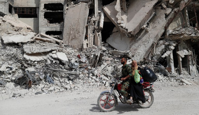 A Syrian Soldier rides his scooter as helps a woman to through a devastated part of the in the Palestinian refugee camp of Yarmouk in the Syrian capital Damascus, Syria, Saturday, Oct. 6, 2018.  The camp, once home to the largest concentration of Palestinians outside the territories housing nearly 160,000 people, has been gutted by years of war.