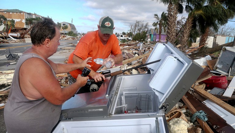 Charles Smith, 56, left, and Lee Cathey, 37, find a few bottles of water in a displaced refrigerator in the middle of U.S. 98 in the coastal township of Mexico Beach, Fla. in the wake of Hurricane Michael.
