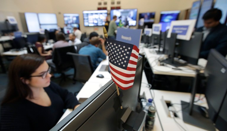 A flag of the United States is shown between monitors as workers sit at their desks during a demonstration in the war room, where Facebook monitors election-related content on the platform, in Menlo Park, Calif.
