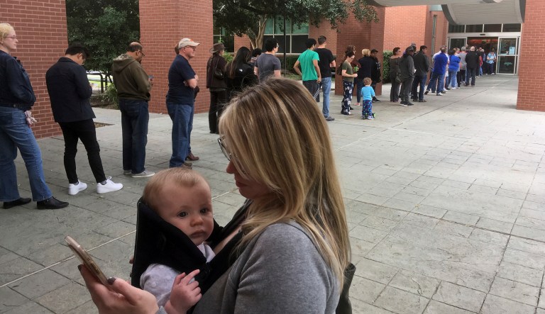 In this Oct. 22, 2018, file photo, Megan Heckel of Plano holds her daughter Lily as they wait in line for early voting outside Maribelle M. Davis Library in Plano, Texas.