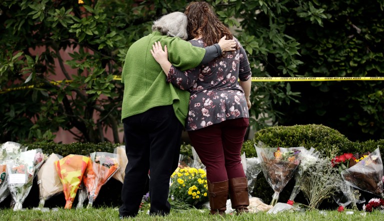 Two people support each other in front of flowers at a makeshift memorial at the Tree of Life Synagogue in Pittsburgh, Sunday, Oct. 28, 2018. Robert Bowers, the suspect in Saturday's mass shooting at the synagogue, expressed hatred of Jews during the rampage and told officers afterward that Jews were committing genocide and he wanted them all to die, according to charging documents made public Sunday.