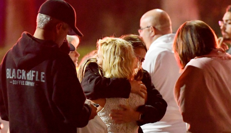 People comfort each other as they stand near the scene Thursday in Thousand Oaks, Calif., where a gunman opened fire Wednesday inside a country dance bar crowded with hundreds of people on "college night," wounding multiple people including a deputy who rushed to the scene.