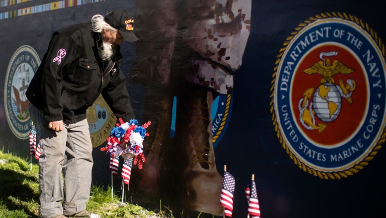 Veteran Patrick Watson places a wreath at the base of a new Mural Arts Philadelphia piece titled "American Tableau" at the Crescenz Veterans Affairs Medical Center.