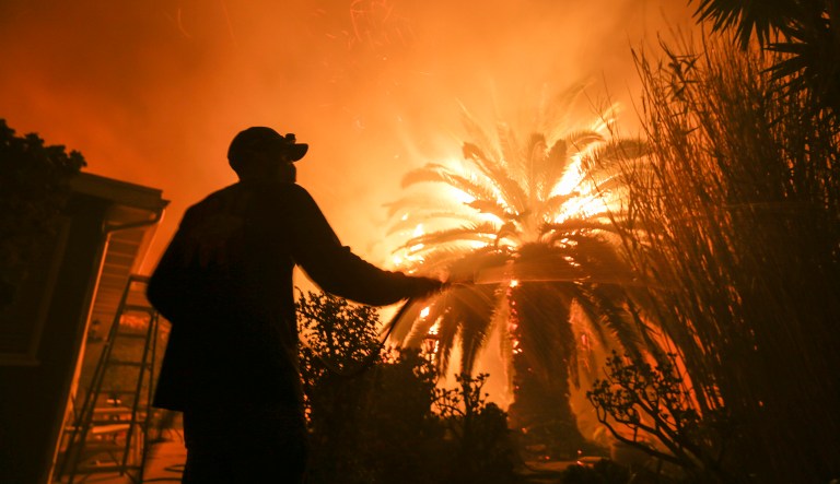 Park Billow, 27, sprays water on the hot spots in his backyard as the Woolsey Fire burns in Malibu, Calif.