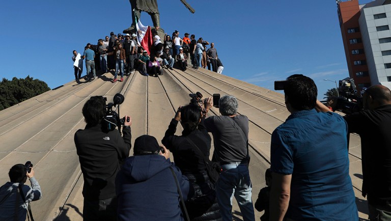 Journalists film people under a statue of indigenous Aztec ruler Cuauhtemoc protesting the presence of thousands of Central American migrants in Tijuana, Mexico.