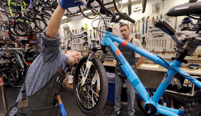In this photo taken Nov. 13, 2018, bicycle mechanic Boo Scott, left, explains a bike component to assembler Alan Everitt in the bike repair department in REI Co-op's flagship store in Seattle. For the fourth consecutive year, REI said that on the popular Black Friday shopping day it will close all 153 stores, process no online payments and pay more than 12,000 employees, encouraging them to recreate outdoors with friends and family. The company calls it #OptOutside. 