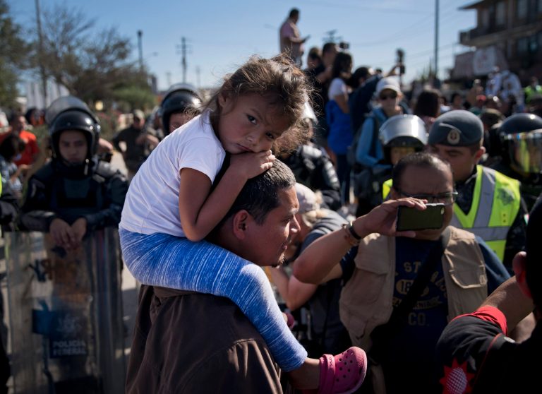 A young migrant sits on a man's shoulders as they join a group of migrants trying to push their way past the Chaparral border crossing in Tijuana, Mexico, Sunday, Nov. 25, 2018. 