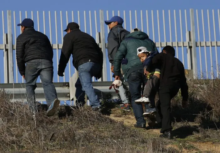 Honduran migrants, one carrying a child, who plan to turn themselves over to U.S. border patrol agents, walk up the embankment after climbing over the U.S. border wall from Playas de Tijuana, Mexico in Tijuana, Mexico, Wednesday, Dec. 12, 2018. The group crossed to apply for asylum.