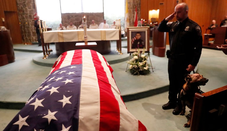 Wounded Dekalb County Police K9 Indi stands by his handler's side as he salutes during funeral service for Dekalb County Police officer Edgar Flores Tuesday, Dec. 18, 2018, in Dunwoody, Ga. Indi was shot while trying to capture the suspect police say shot and killed Flores after making a traffic stop in Decatur, Ga., on Dec. 13, 2018.